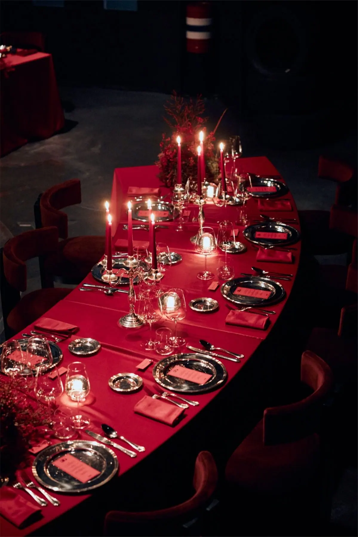 A curved table dressed in red, set with silver plates and lit by tall candles.
