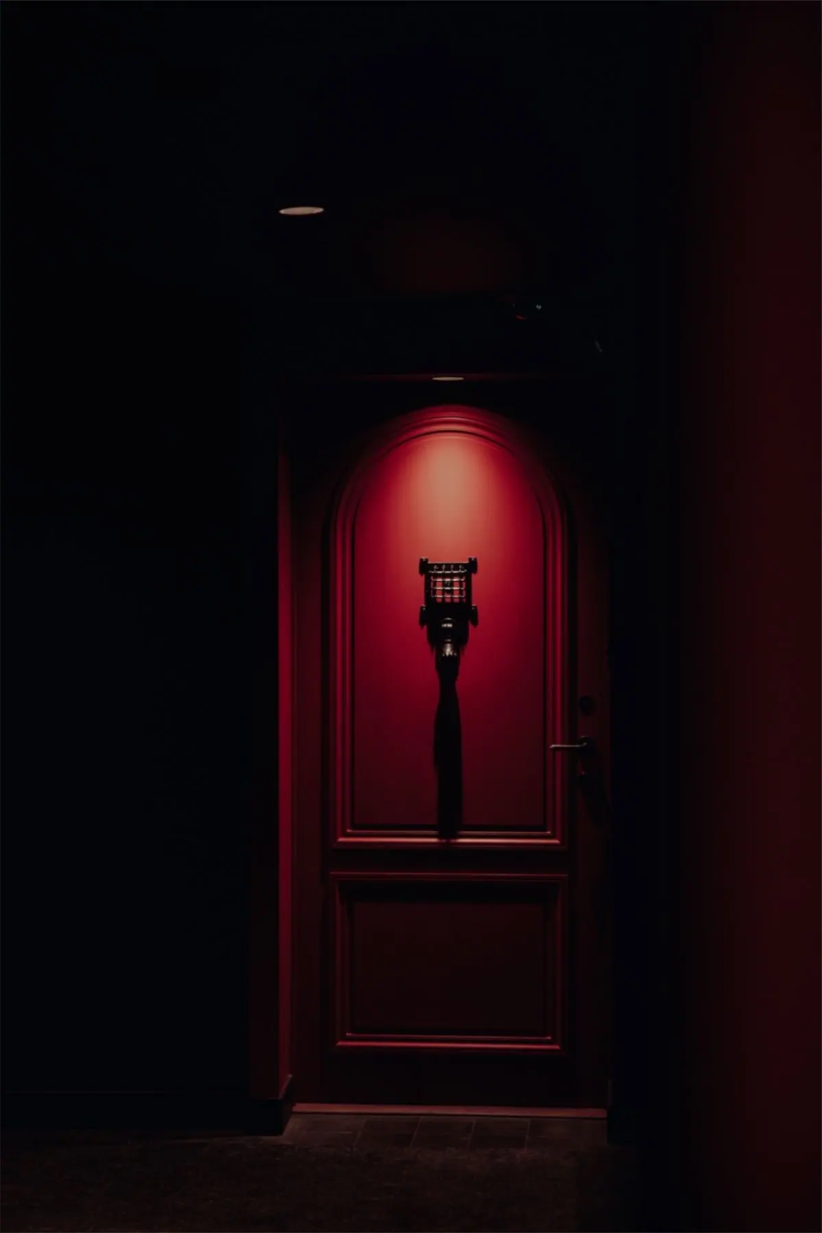 A red arched door lit by a single spotlight in a dark corridor.