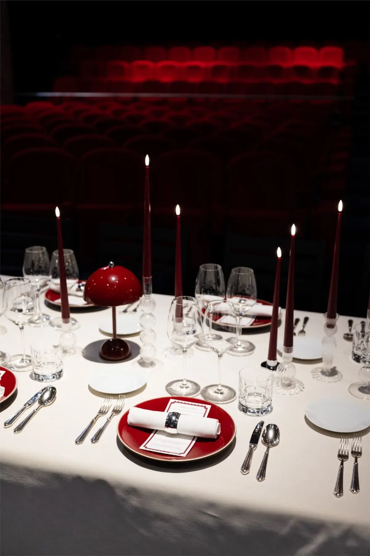 A table laid with white linen and burgundy candles in front of rows of red theatre seats.