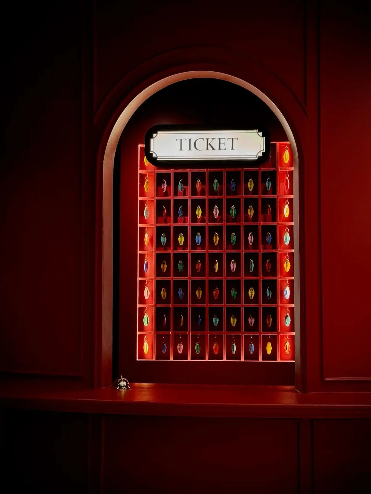 A ticket window in a red panelled wall, with rows of coloured key fobs behind it.